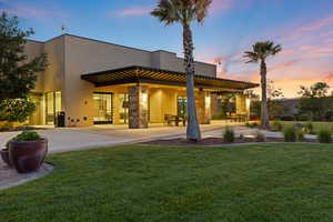 Rear view of property featuring stucco siding, a lawn, stone siding, and a patio