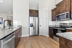 Kitchen featuring stainless steel appliances, light wood-style flooring, a sink, dark brown cabinets, and light stone counters
