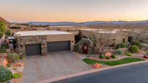 Pueblo-style home featuring a mountain view, stone siding, a garage, stucco siding, and decorative driveway