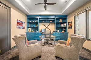 Carpeted office featuring built in shelves, ornamental molding, a ceiling fan, and a tray ceiling
