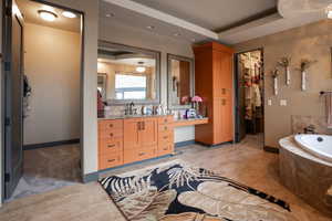 Bathroom with a walk in closet, a garden tub, vanity, and baseboards