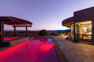 Pool at dusk with fence, a pool with connected hot tub, and a mountain view