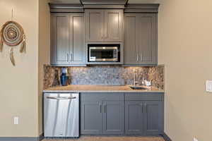 Bar featuring baseboards, appliances with stainless steel finishes, tasteful backsplash, and a sink