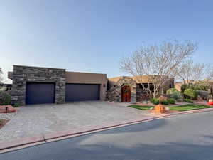 View of front of house with stucco siding, stone siding, decorative driveway, and a garage