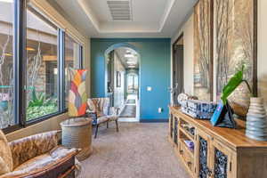 Living area with carpet, a tray ceiling, visible vents, arched walkways, and baseboards