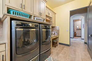 Washroom with washing machine and clothes dryer, arched walkways, light wood-type flooring, baseboards, and cabinet space