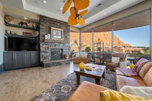 Living area with a ceiling fan, a stone fireplace, wood finished floors, a raised ceiling, and visible vents