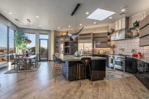 Kitchen featuring wall chimney range hood, high end appliances, light wood-style flooring, a kitchen bar, and visible vents