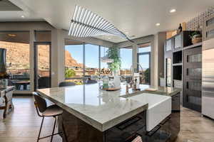 Kitchen featuring recessed lighting, a sink, wood-type flooring, light stone countertops, and a center island with sink