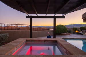 Pool at dusk featuring a fire pit, a mountain view, a fenced in pool, and an in ground hot tub