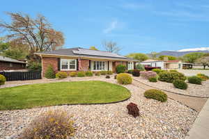View of front of home with roof mounted solar panels, a front lawn, brick siding, and fence
