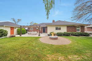 Rear view of house featuring a lawn, a fire pit, brick siding, and a patio