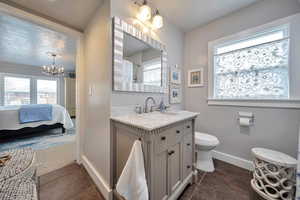 Ensuite bathroom featuring tile patterned floors, vanity, baseboards, toilet, and a notable chandelier