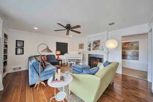 Living area featuring ceiling fan, a lit fireplace, dark wood finished floors, ornamental molding, and visible vents