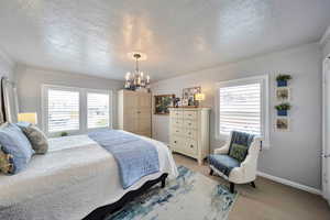 Bedroom with a textured ceiling, a chandelier, light colored carpet, and multiple windows