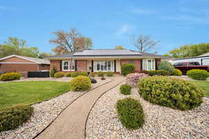 Ranch-style home with a front lawn, brick siding, fence, and roof mounted solar panels