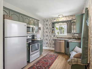 Kitchen featuring stylish wallpapered walls, appliances with stainless steel finishes, and stylish green cabinetry.