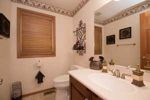 Bathroom featuring toilet, vanity, visible vents, and baseboards