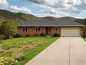 Single story home with brick siding, a garage, driveway, a mountain view, and a front yard
