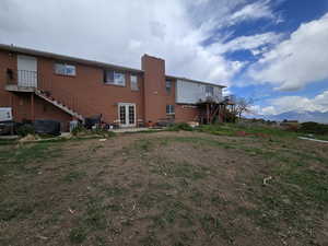 Rear view of property featuring a chimney, a patio area, stairway, french doors, and brick siding