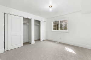 Unfurnished bedroom featuring baseboards, visible vents, carpet, and two closets
