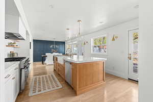Kitchen with open shelves, a sink, an island with sink, light wood-style floors, and stainless steel appliances
