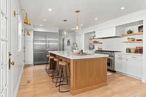 Kitchen featuring tasteful backsplash, open shelves, high end appliances, a breakfast bar, and custom range hood