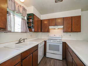 Kitchen featuring white appliances, under cabinet range hood, light countertops, a sink, and dark wood-type flooring