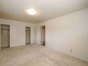 Unfurnished bedroom with visible vents, multiple closets, and light carpet