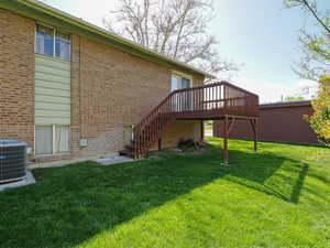 Back of property with a deck, a lawn, stairway, central AC unit, and brick siding