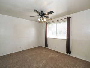 Carpeted empty room with visible vents and a ceiling fan