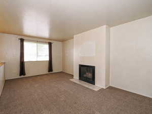 Unfurnished living room featuring a fireplace with flush hearth and carpet flooring