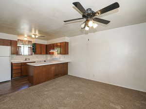 Kitchen featuring white appliances, under cabinet range hood, light countertops, dark colored carpet, and a peninsula
