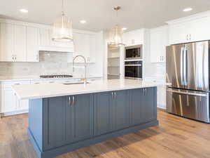 Kitchen featuring tasteful backsplash, a sink, white cabinetry, light countertops, and appliances with stainless steel finishes