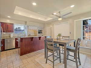 Dining area with a tray ceiling, stone tile flooring, a ceiling fan, and recessed lighting