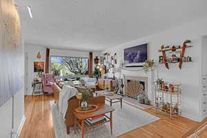 Living room view from front door featuring original wood floors, a textured ceiling, and a fireplace with raised hearth