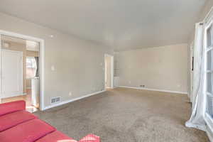 Unfurnished living room with visible vents, carpet flooring, and baseboards