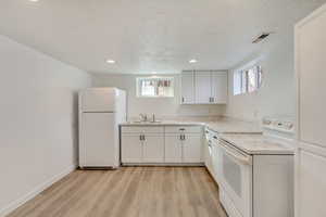 Kitchen featuring white cabinets, light wood-style flooring, a sink, visible vents, and white appliances