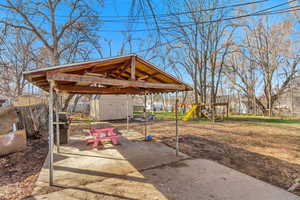 View of patio featuring an outdoor structure, a playground, a gazebo, a shed, and fence
