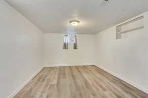 Below grade area with visible vents, light wood-type flooring, a textured ceiling, and baseboards