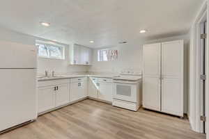 Kitchen featuring white cabinetry, a sink, visible vents, light wood-type flooring, and white appliances