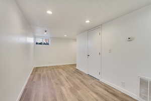 Basement with baseboards, light wood-type flooring, visible vents, and recessed lighting