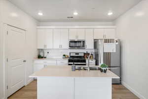 Kitchen with light wood-style flooring, white cabinets, a sink, stainless steel appliances.