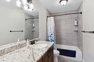 Bathroom with shower / bathtub combination with curtain, vanity, and toilet