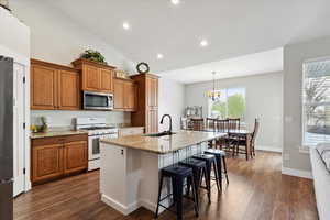 Kitchen with white gas range oven, brown cabinets, stainless steel microwave, a sink, and plenty of natural light