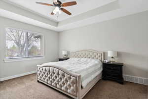 large primary bedroom with custom box tray ceilings and oversized window