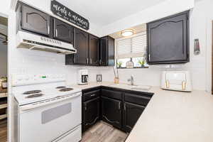 Kitchen with a sink, under cabinet range hood, white electric stove, light wood-type flooring, and light countertops