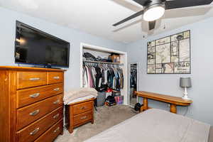 Carpeted bedroom with ceiling fan and a closet