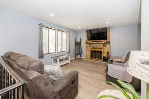 Living room with recessed lighting, light wood-style flooring, and a stone fireplace