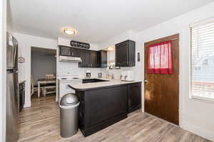 Kitchen with white electric stove, a peninsula, under cabinet range hood, and plenty of natural light